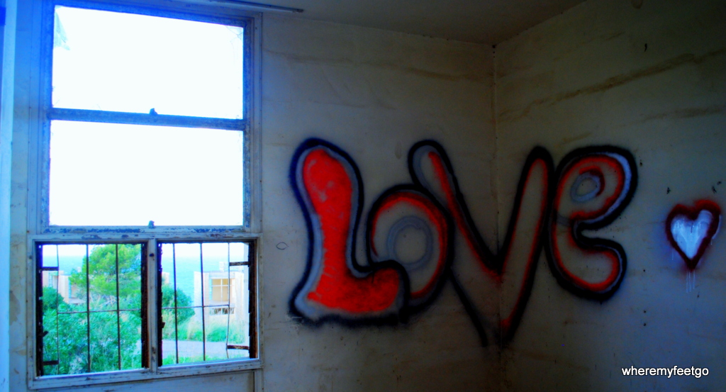 the word "LOVE" written in bubble letters with spray-paint on two walls. the "v" is divided in half by the corner seem where the wall joints the other.